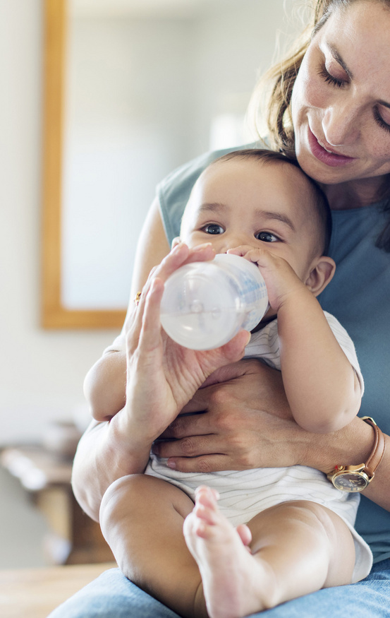 baby drinking milk from bottle on moms lap